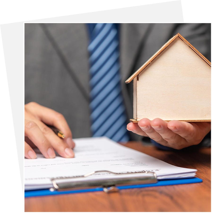 A person holding a small house and writing on paper.